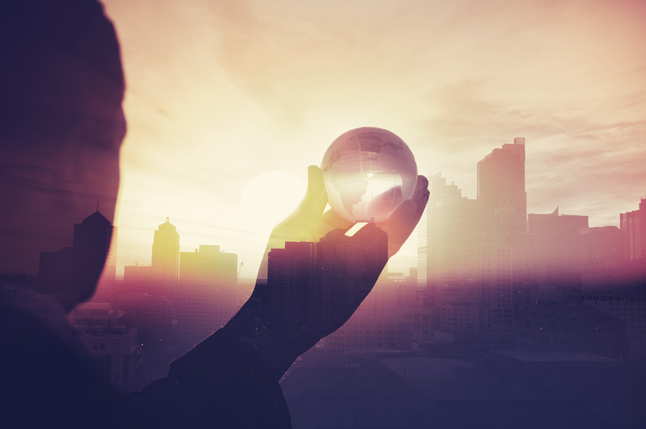 Business man holding globe with cityscape montage behind.