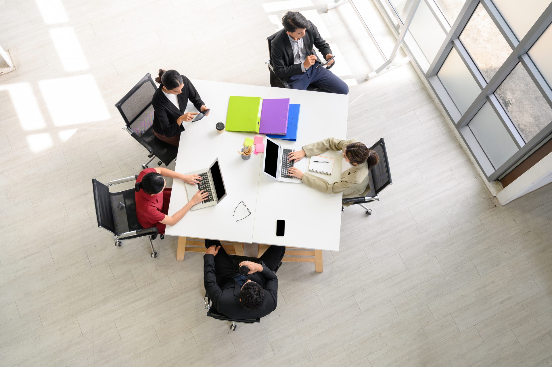 Top-down view of five business professionals working on different devices